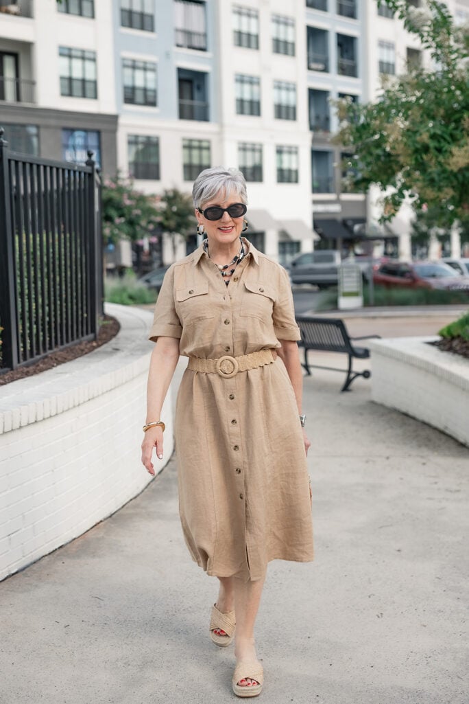 Beth Djalali in a belted khaki safari linen shirtdress with platform espadrilles and a black-and-white beaded necklace — natural fiber summer style over 50