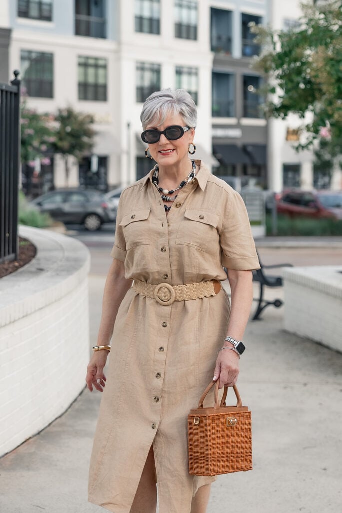 Beth walking in a linen safari shirtdress styled with raffia platform sandals and a gold bangle