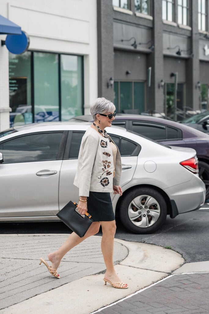 Beth walking in Dunwoody wearing an embroidered linen jacket, black Bermuda shorts, and nude kitten-heel sandals