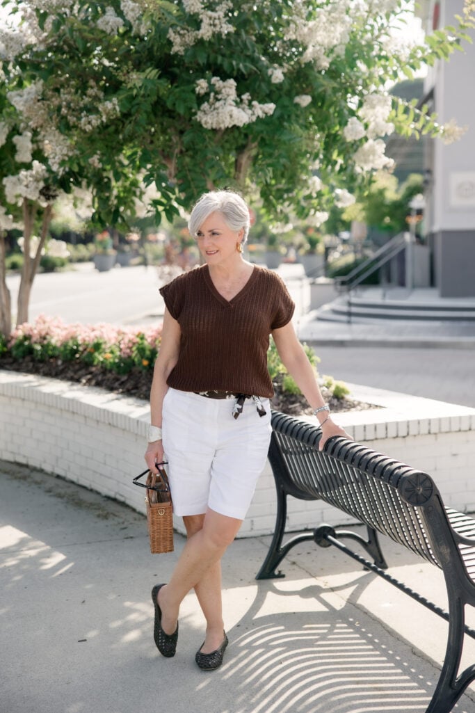 Beth Djalali wearing white linen Bermuda shorts with a brown knit top and scarf belt — the tailored short trend for summer 2026