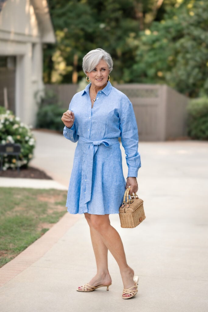 Beth wearing a blue striped linen shirtdress with a tie waist, raffia kitten heels, and a wicker box bag