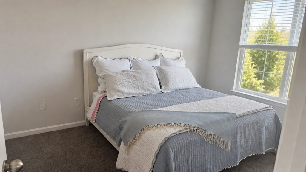 White bedframe dressed with a cornflower blue pom pom quilt and white scalloped quilted bedding in a classic blue and white bedroom