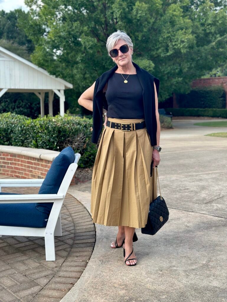Black top with khaki pleated midi skirt and black belt, a summer color combination for women over 50