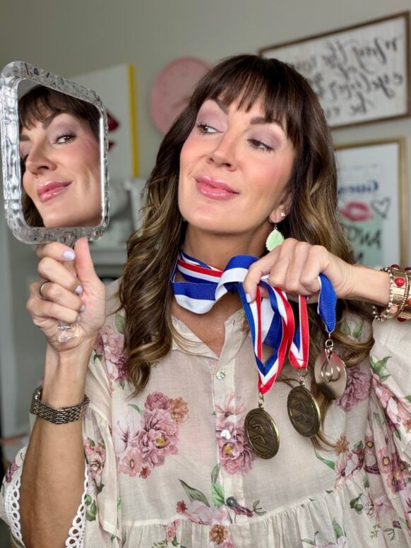 Woman over 50 in bathroom mirror holding her best beauty products of 2026