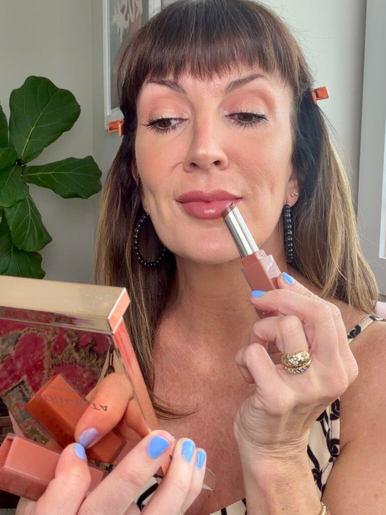Applying a hydrating pinky-brown lip gloss stick to finish a quick makeup look.