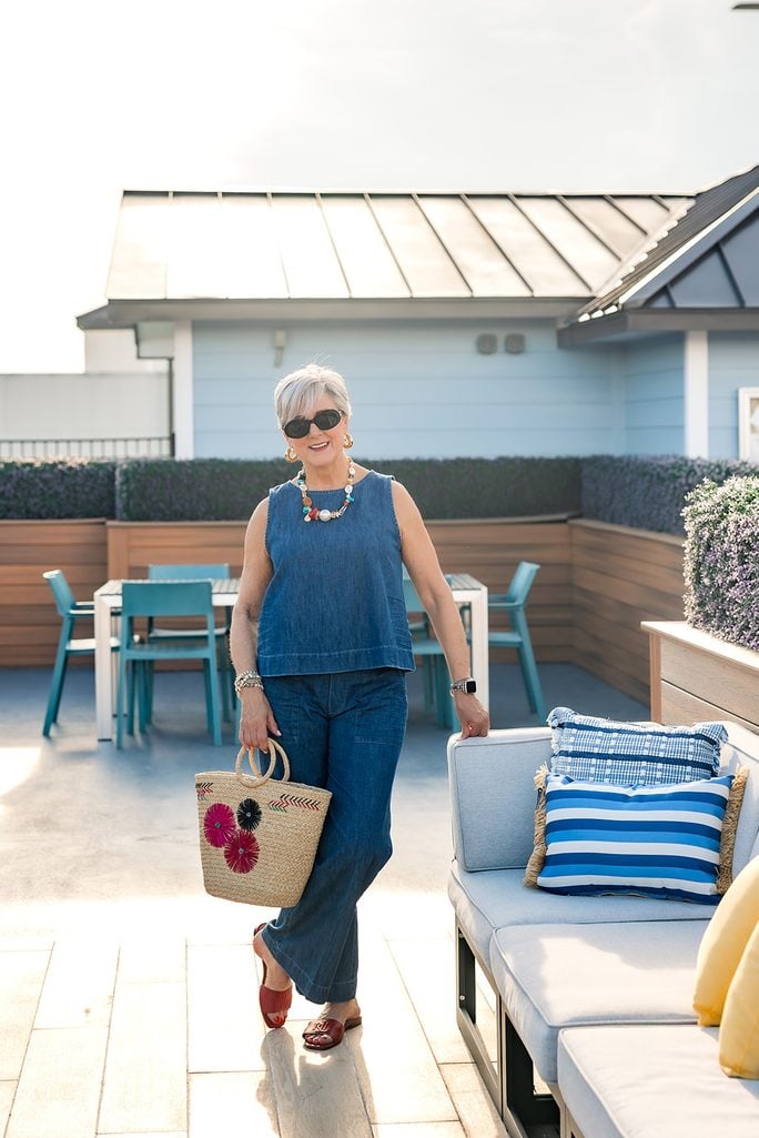 Denim outfit for women over 50 with a floral straw tote and red slide sandals