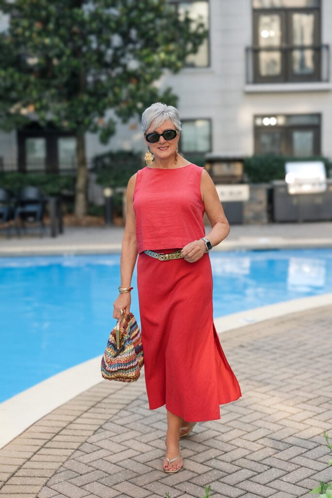Woman over 50 in a coral linen Gap set carrying a woven kisslock handbag by the pool