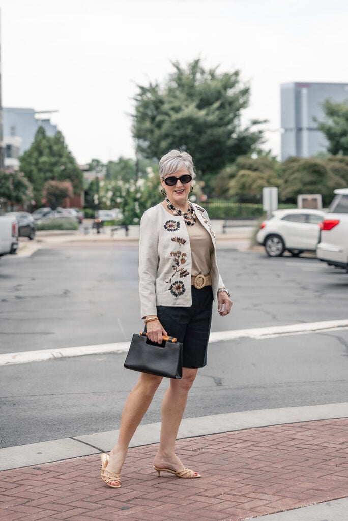Woman styling a linen collarless embroidered jacket with black shorts and kitten heels