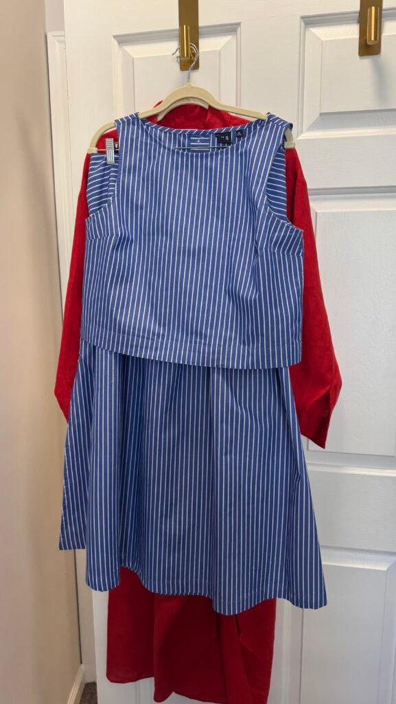 Silver-haired woman in a blue-and-white striped drop-waist skirt set with a cable knit over her shoulders, tan espadrille wedges, and a red bag — a daytime reunion outfit for women over 50.