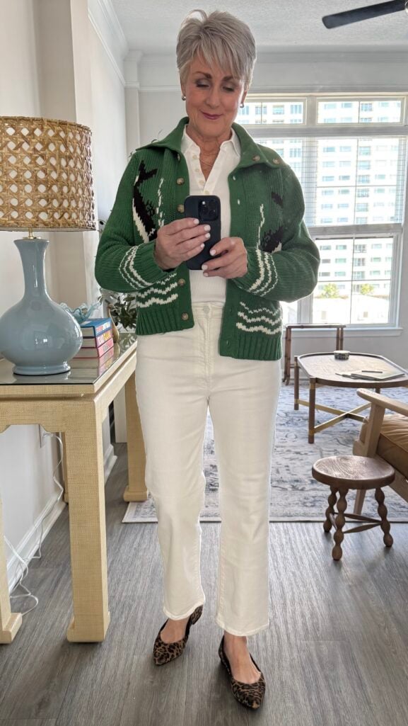 Woman over 50 in a green patterned cardigan, cream jeans, and leopard flats — an easy travel outfit for a high school reunion weekend.