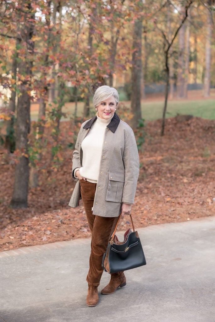 Beth of Style at a Certain Age looking off to the side in a houndstooth barn jacket, cream turtleneck, and brown corduroy pants, carrying a black leather tote