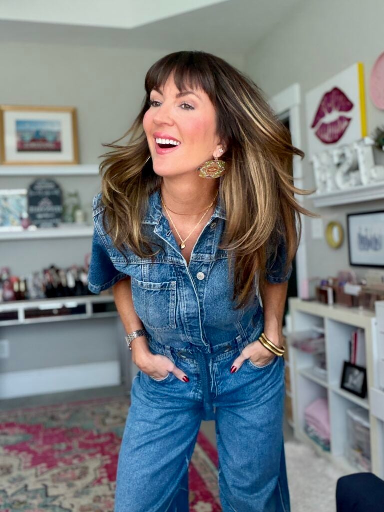 Woman over 50 in a denim jumpsuit sharing her fall beauty must-haves