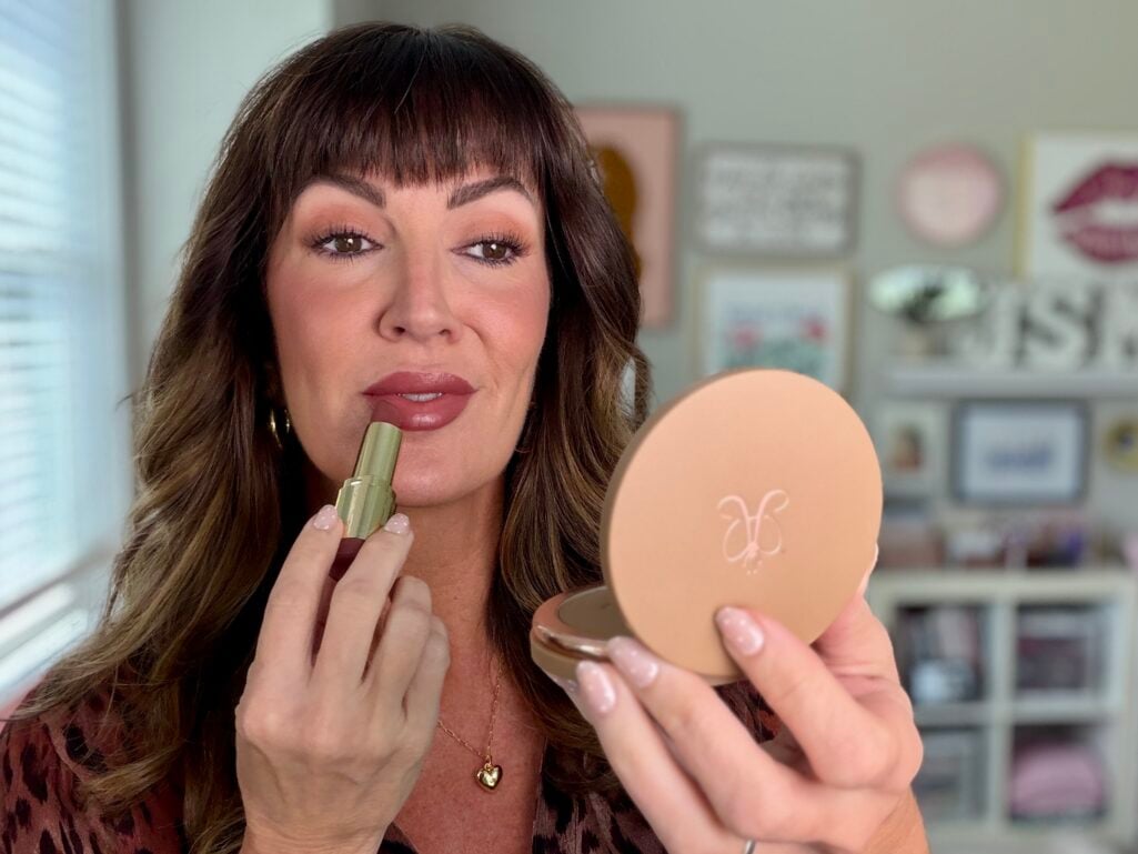 Applying Milani Color Statement lipstick with a bronzer compact mirror in hand