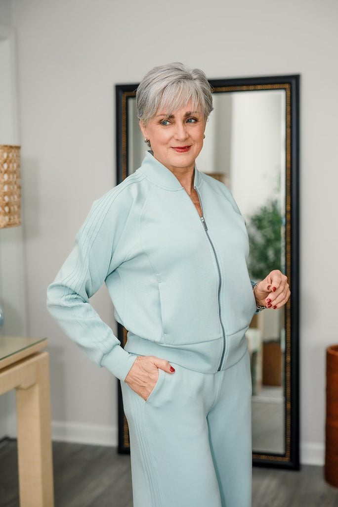  Beth Djalali at home in a pale aqua Spanx Pintuck Track Jacket and matching wide-leg pants with red lipstick and gold earrings