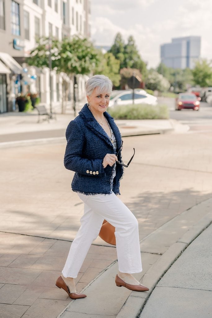 Beth in a navy tweed blazer and printed vest styled with white jeans and cognac accessories for fall