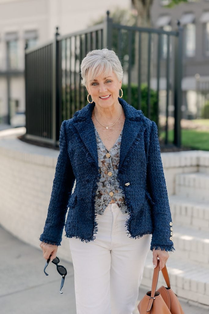 Beth styling white jeans for fall with a navy tweed blazer, printed vest, cognac handbag, and brown flats