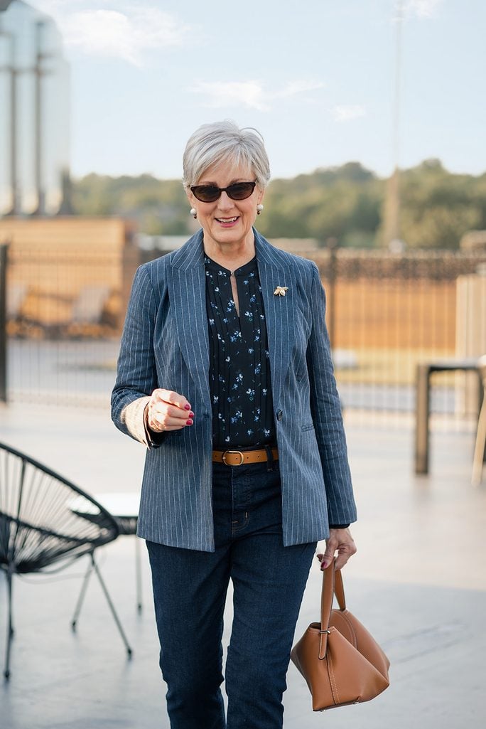 Beth Djalali in a blue pinstripe blazer over a navy floral pintucked blouse with dark jeans, a cognac belt and a cognac handbag