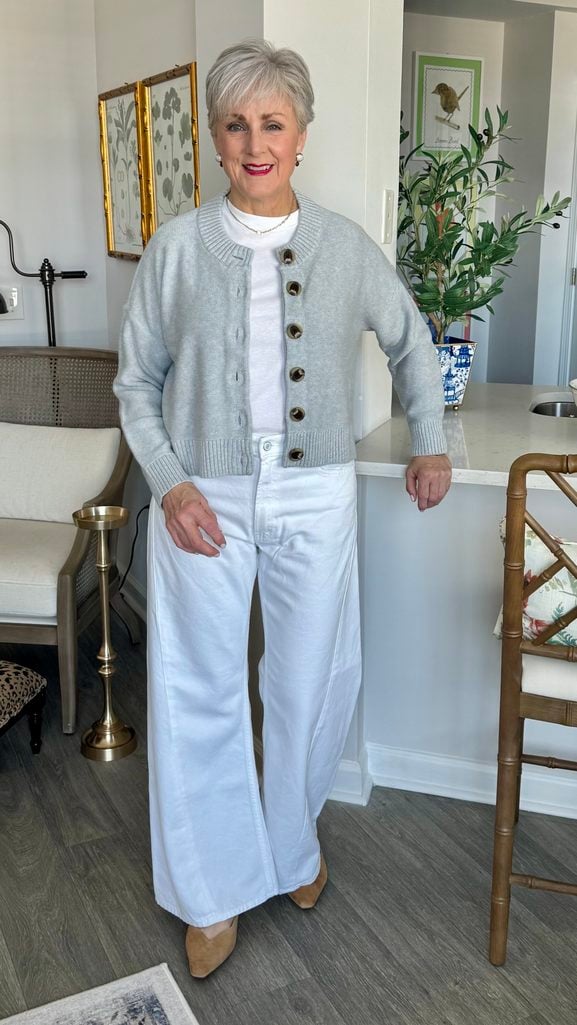 Beth wearing wide-leg white jeans with a grey cropped cardigan, white tee, and tan suede mules for fall
