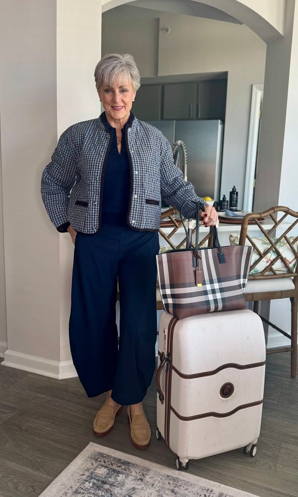 Beth Djalali in a gingham quilted jacket, navy sweater and navy barrel pants with a check tote and cream suitcase