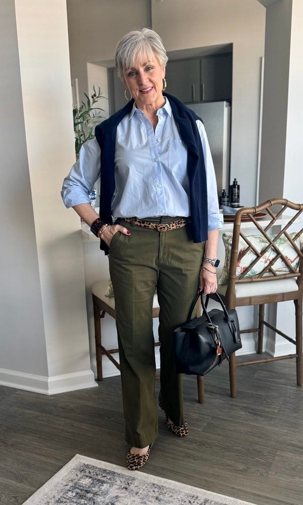Light blue oxford shirt and olive wide-leg chinos with a navy sweater over the shoulders, leopard belt and leopard flats