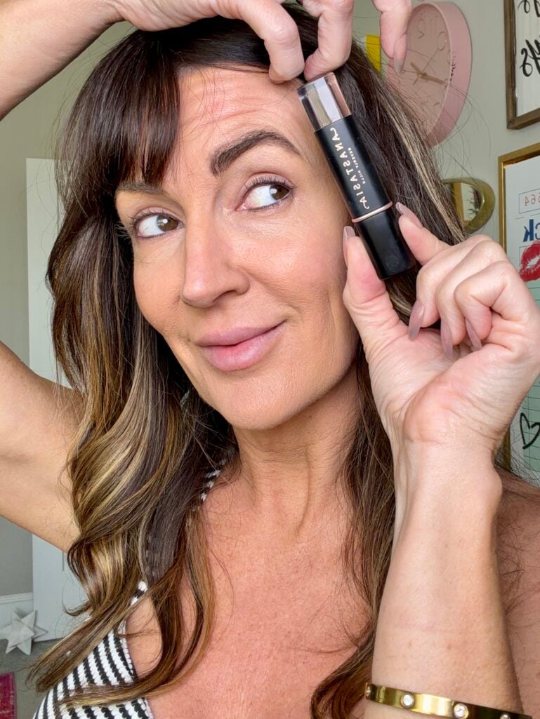 Jennifer Duvall holding Anastasia Beverly Hills Volumizing Tinted Brow Gel next to her full, fluffy brow