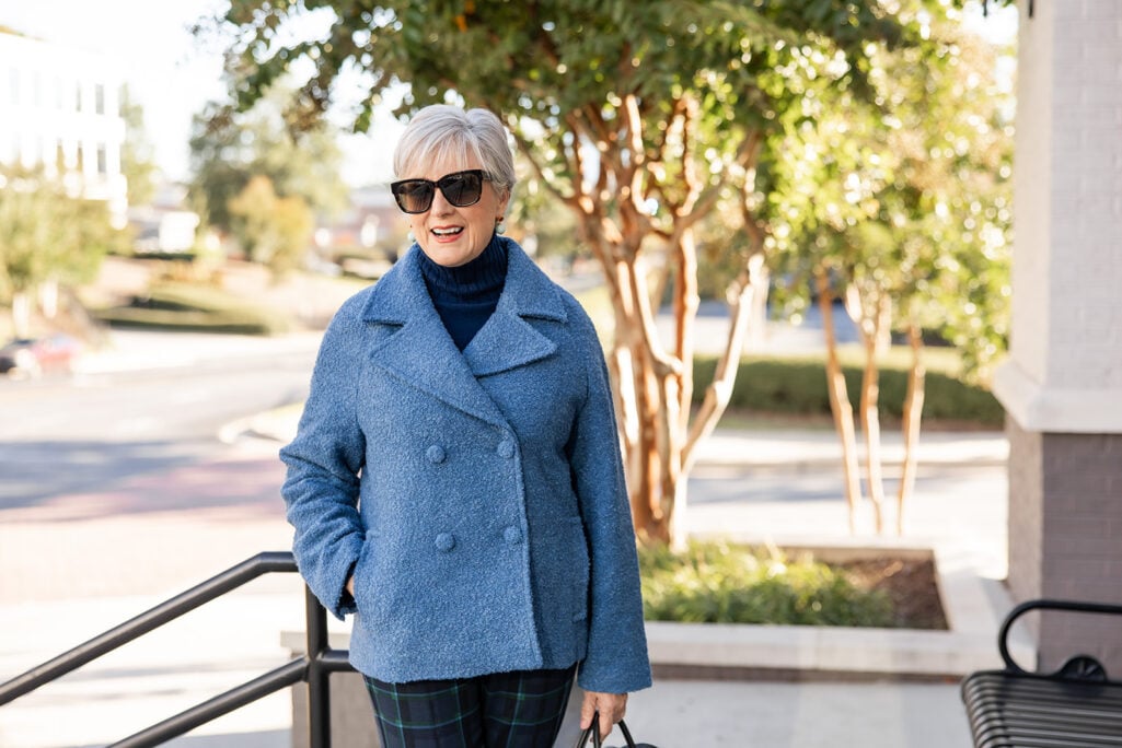 Beth Djalali in a blue bouclé double-breasted jacket over a navy cashmere turtleneck, with drop earrings and black sunglasses.