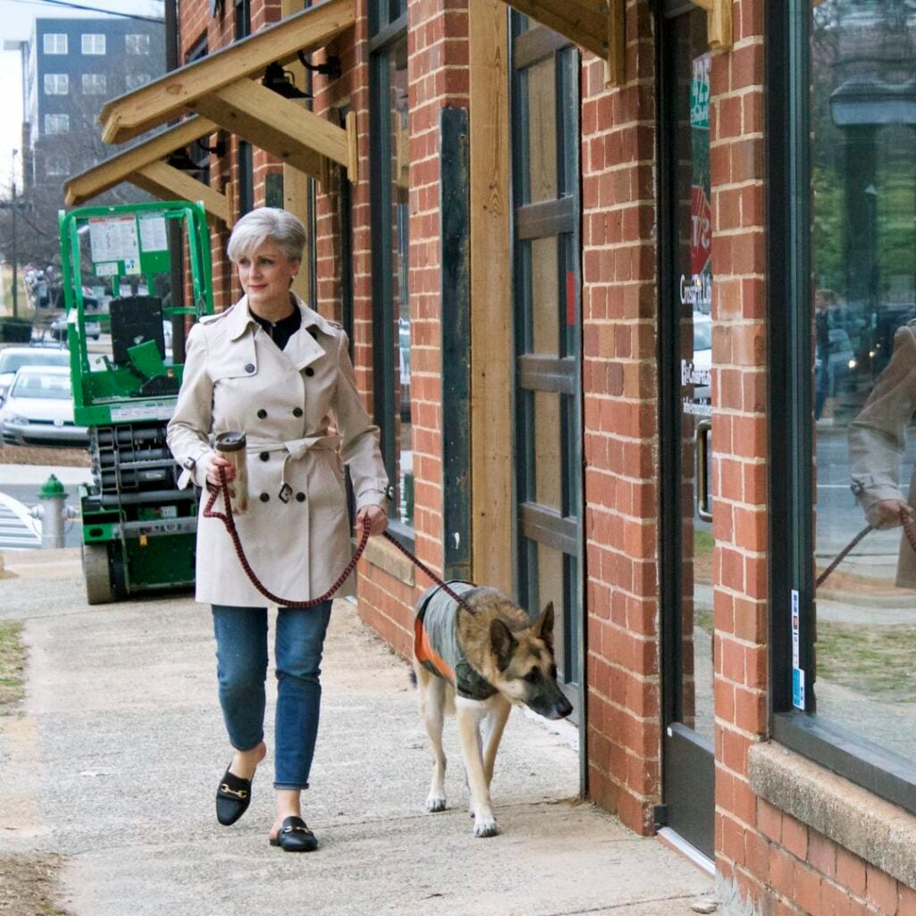 Best fall jackets for women over 50: a classic knee-length trench coat with light-wash jeans and horsebit mules