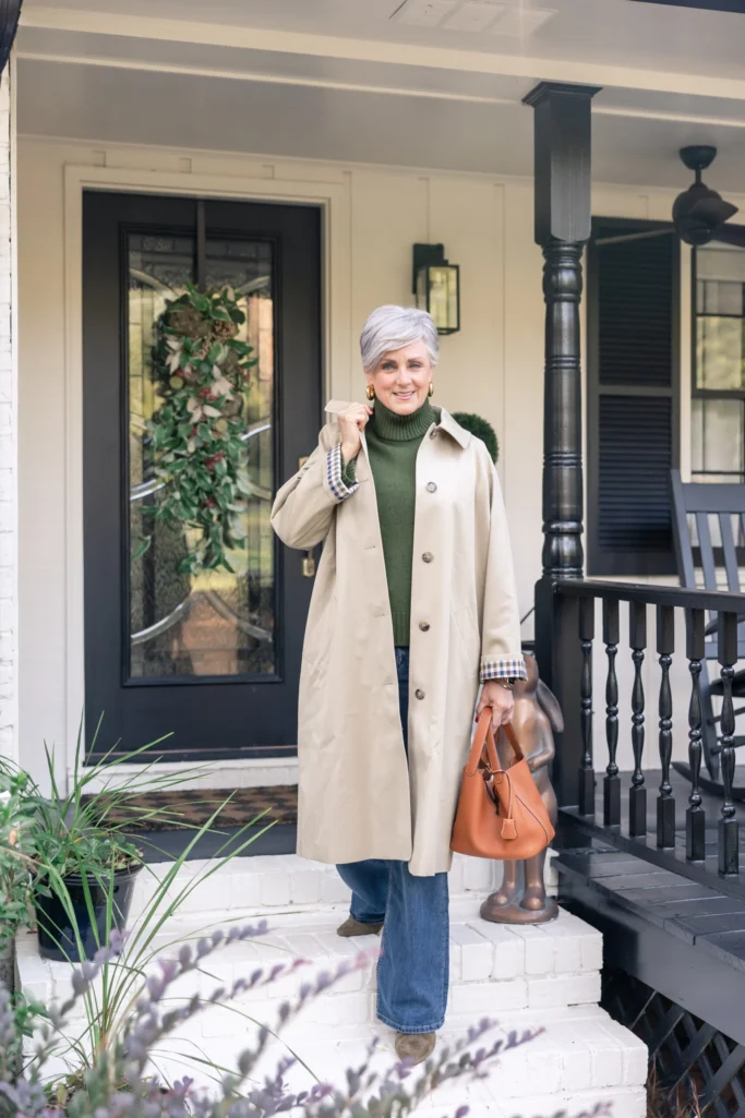 Trench coat worn open to show a plaid lining, with a green sweater and wide-leg jeans