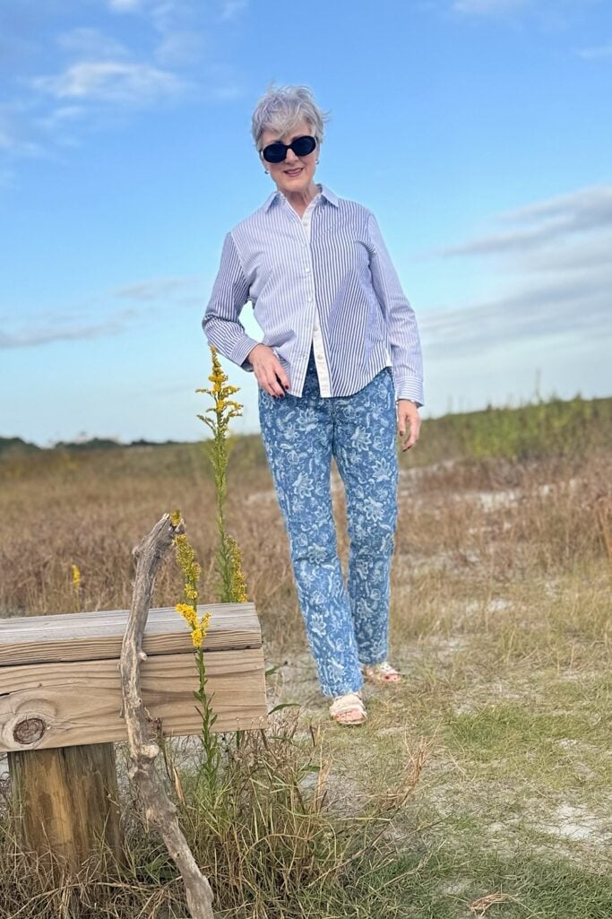 Beth in a blue striped button-down and floral jacquard jeans beside goldenrod and driftwood near the marsh on St. Simons Island