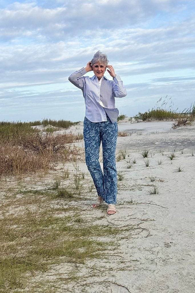 Beth laughing on the dunes in a blue striped button-down and blue floral jacquard flare jeans